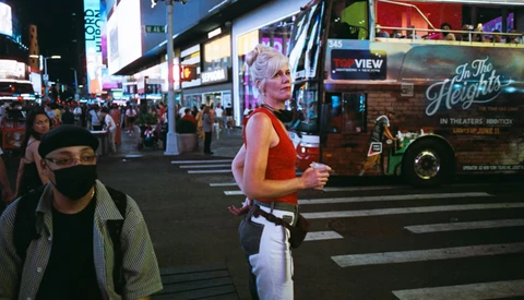 Jogger in red tank top and white pants running across a crosswalk in a busy urban theater district at night.