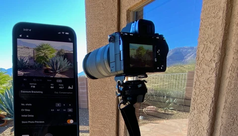 Smartphone displaying exposure bracketing settings next to a mirrorless camera mounted on a tripod.