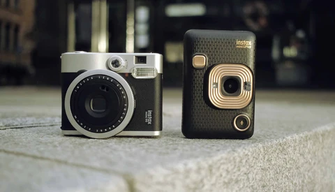 Two vintage instant cameras displayed side by side on a concrete surface.
