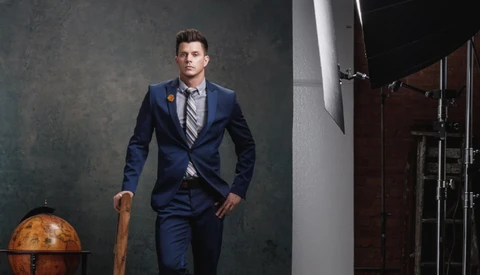 Man in navy blazer and striped tie standing in studio with globe and industrial backdrop.