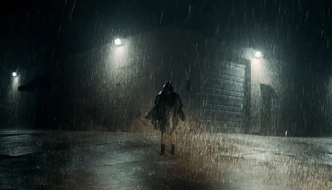 Solitary figure standing in heavy rain on a wet urban street under streetlights.