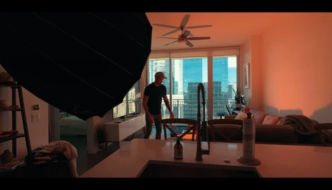 Studio interior with warm orange-toned lighting, featuring a person standing near large windows overlooking a city skyline.
