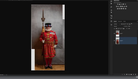 Man in elaborate red ceremonial uniform with feathered hat, holding ornamental staff, posed against neutral backdrop.