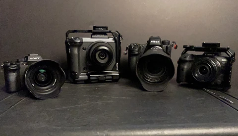 Four digital cameras of varying sizes arranged in a line on a dark surface.