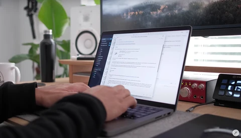 Photographer working at desk with laptop displaying editing software and dual monitors in a creative workspace.