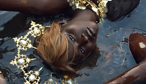 Woman with bronze skin submerged in water wearing ornate gold jewelry and black fabric.