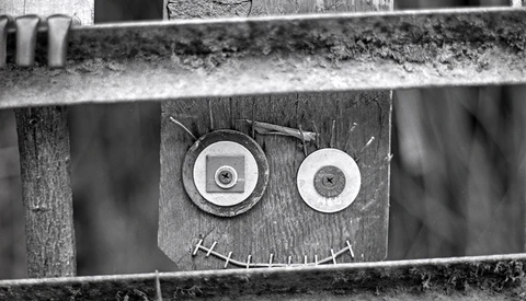 Found-object art face made from circular metal discs and stitched line on wooden boards.