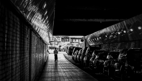 Solitary figure walking through narrow urban alley lined with parked cars at night.