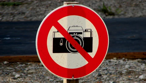 Red and white prohibition sign with a camera crossed out by a diagonal line.