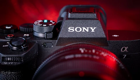 Sony α7 mirrorless camera with flash and lens against deep red backdrop.