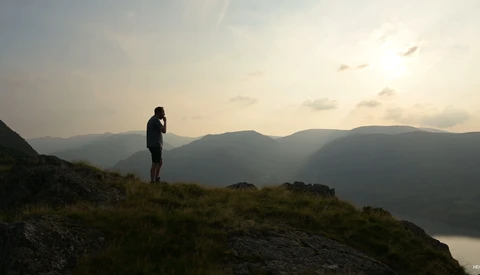 Silhouetted hiker standing on a rocky outcrop overlooking a misty mountain valley at sunset.