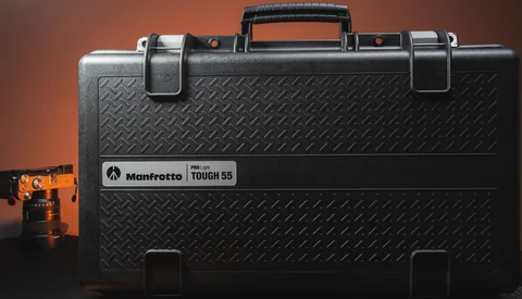 Manfrotto Tough 55 hard case with orange camera head shown on warm brown background.