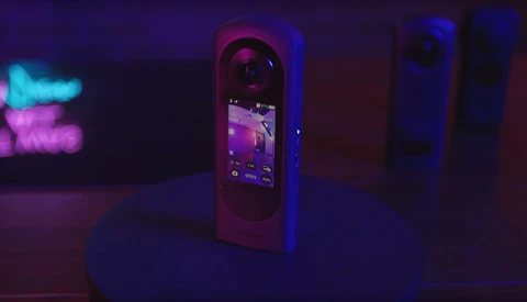 Smartphone displaying a purple-toned interface surrounded by neon blue and pink lighting in a dark environment.