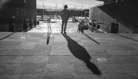 Silhouetted figure standing on a concrete plaza with a dramatic shadow cast across the ground.