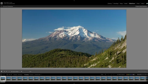 Snow-capped volcanic mountain rising above forested foothills under clear blue sky.