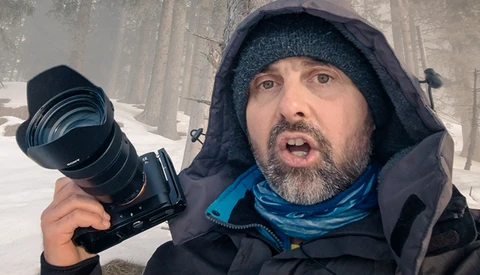 Photographer holding a telephoto lens in snowy conditions while wearing winter gear.