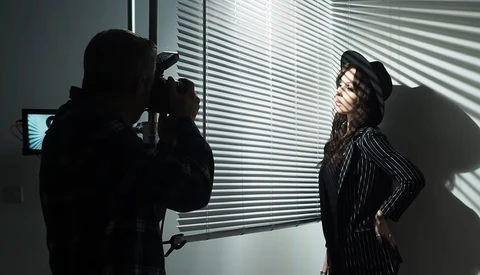 Photographer shooting a portrait of a woman in a pinstriped suit against a window with venetian blinds.