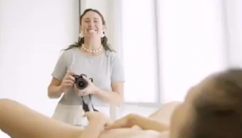 Photographer holding a camera while instructing a student in a bright studio setting.