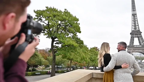 Photographer capturing a couple posing together with an iconic iron tower in the background.