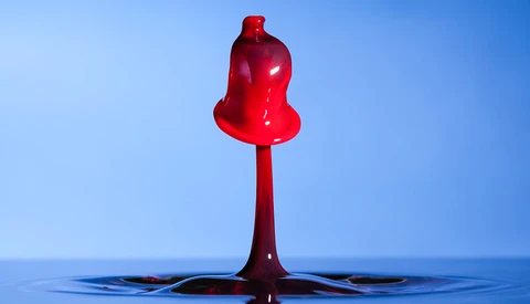 Red liquid drop suspended above water surface against blue background.