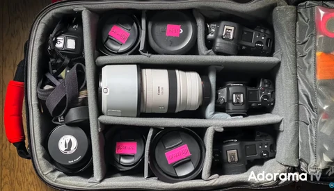 Organized camera gear in a gray divider insert, including lenses, wireless microphone, flash units, and accessories with pink accent labels.