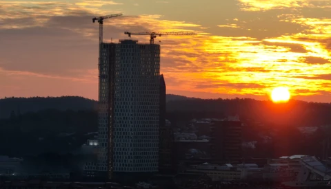Tall residential tower under construction at golden hour, silhouetted against dramatic sunset sky with construction cranes visible at top.