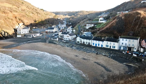 Coastal village nestled between dramatic cliffs with beachfront buildings and incoming waves.