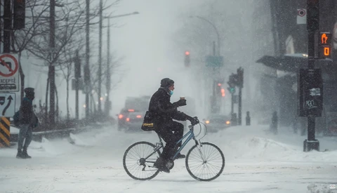 Cyclist riding through heavy snow on an urban street during a blizzard.