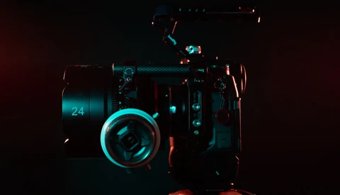 Professional cinema camera lit with cyan and red neon glow against dark background.
