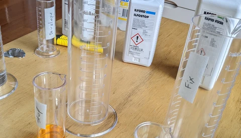 Laboratory cylinders and bottles with chemical solutions arranged on a wooden workbench.