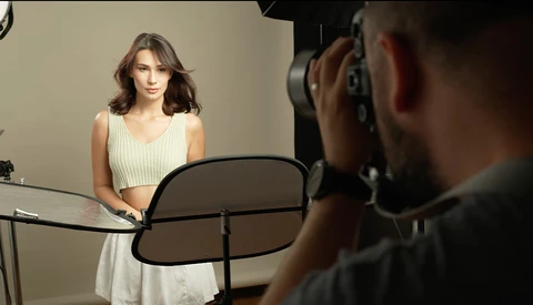 Photographer holding a camera on a reflector during a studio portrait session with a woman in a cream-colored dress.
