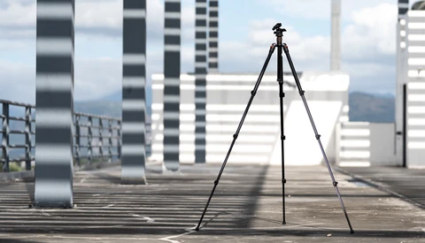 Camera tripod set up on a rooftop with modern skyscrapers and mountains in the background.