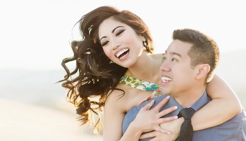 Two people smiling and embracing outdoors against a bright, overexposed sky.