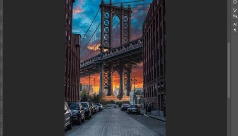 Urban street framed by buildings with suspension bridge and dramatic sunset sky at dusk.