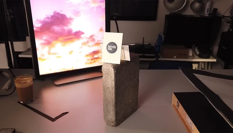 Concrete block with white label on studio desk displaying colorful sunset sky on monitor.