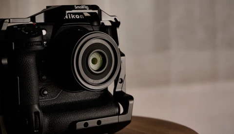 Black Nikon DSLR camera with Smallrig cage mounted on wooden surface against blurred background.
