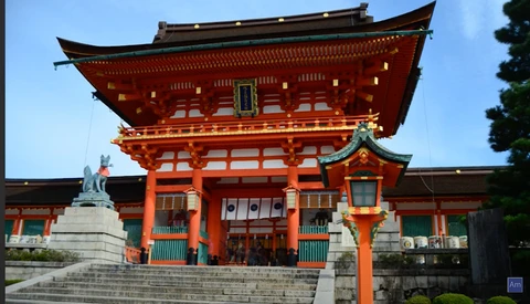 Bright red traditional Japanese temple gate with ornate curved roofing and golden accents under clear blue sky.