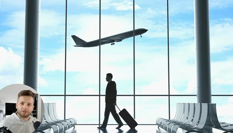 Businessman walking through airport terminal with luggage past a large window showing an airplane taking off.