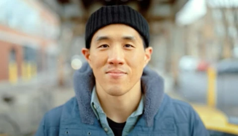 Portrait of a man wearing a black beanie and blue jacket against a blurred urban street background.