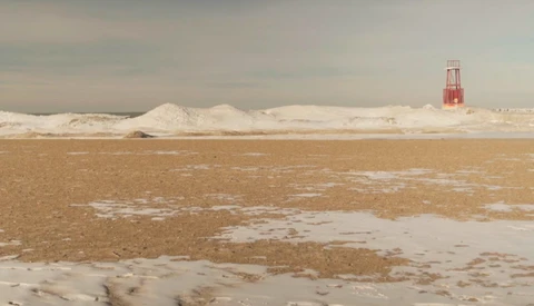 Frozen lake with industrial salt mounds and red navigation tower in winter landscape.