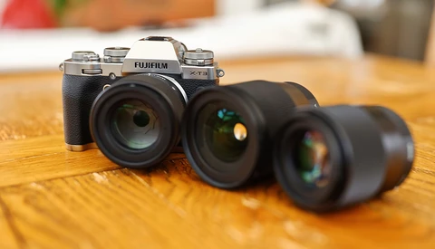 Fujifilm X-T5 camera with three interchangeable lenses arranged on wooden surface.