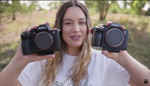 Photographer holding two Sony Alpha mirrorless cameras side-by-side outdoors.