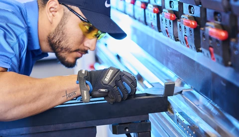 Technician in work gloves inspecting equipment panel with illuminated controls and indicators.