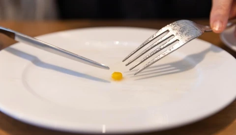 Fine dining plating technique with a single quail egg centered on a white plate, positioned between fork and knife.