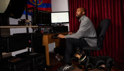 Man working at a computer desk in a content creation studio with professional lighting and red curtains.