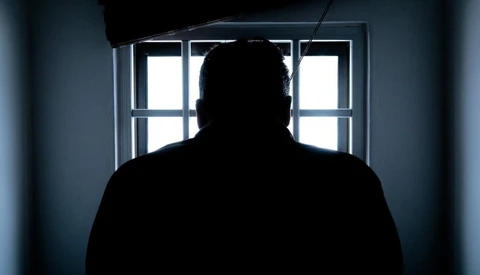 Silhouetted figure facing a bright window with gridded panes in a dimly lit interior space.