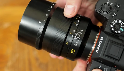 Photographer's hand holding a telephoto lens mounted on a DSLR camera body against a wooden surface.