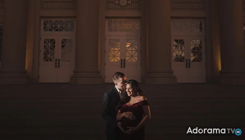 Couple embracing in front of an ornate building entrance at night with warm uplighting.