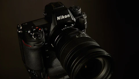 Black Nikon DSLR camera with telephoto lens mounted, photographed against dark background.