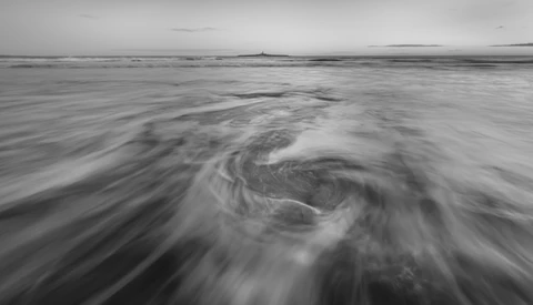 Swirling ocean water with long exposure motion blur creating spiral patterns across the frame.